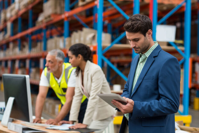 Warehouse managers in a warehouse going over order processing on their laptops and tablets